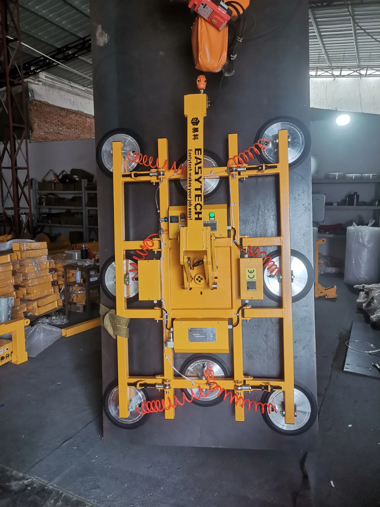 Factory photograph of the upright assembly suspended from a hoist; the lifting arm, frame and eight pads remain visible.